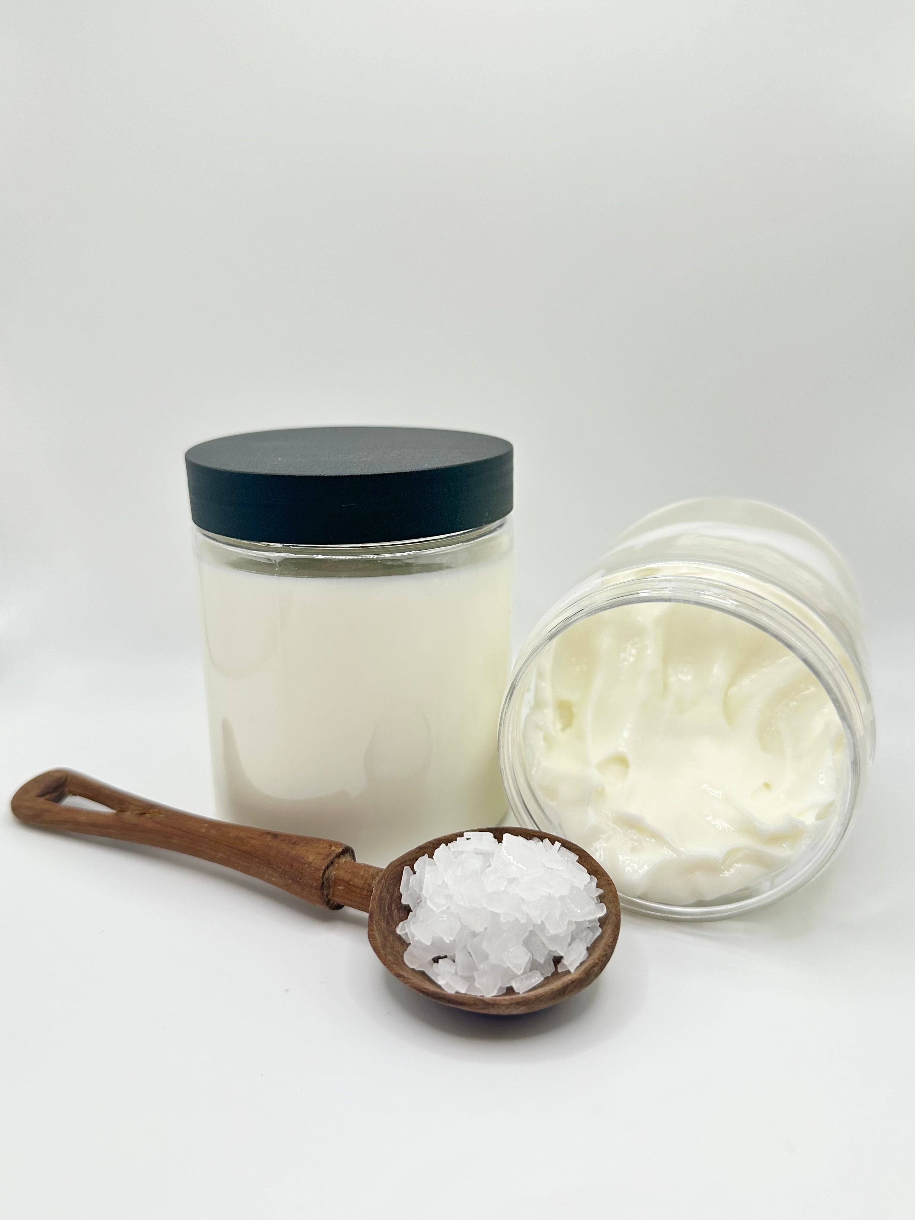 two jars of white lotion. with a wooden spoon with magnesium flakes in it. On a gray background.