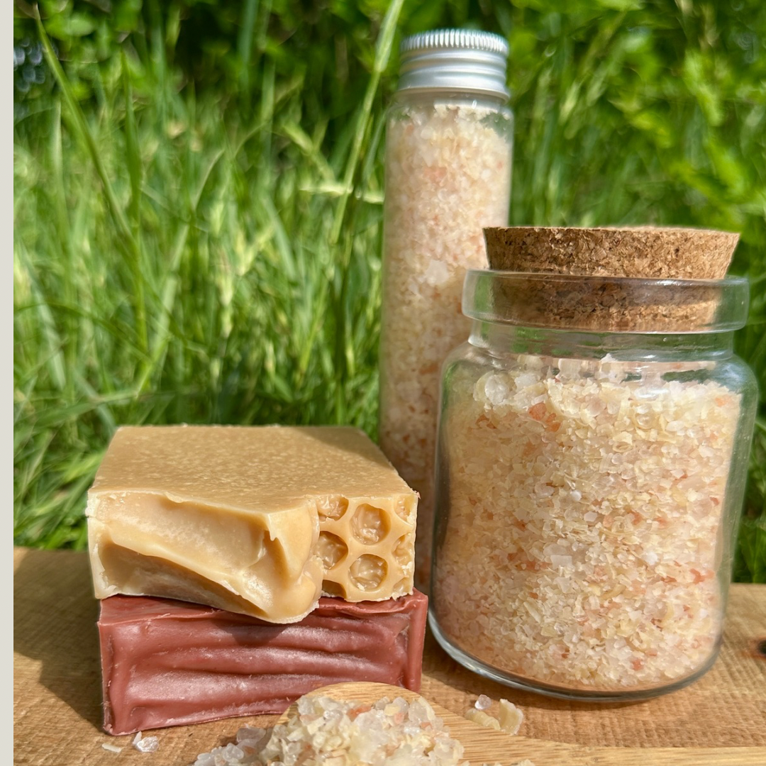 Two bars of soap and two jars on a wooden surface with grass in the background