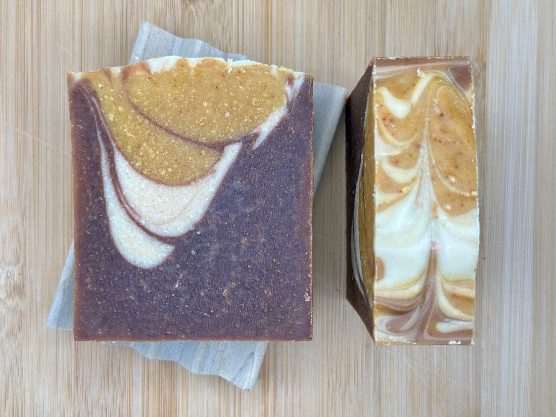 Two soap bars with brown, white, and gold color on a wooden surface
