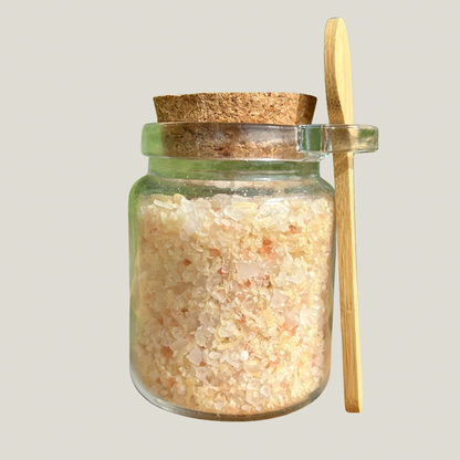 Glass jar with cork lid and wooden spoon filled with a bath salt on a gray background